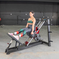 Thumbnail for Woman in green top and patterned leggings using a hack squat machine with weights.
