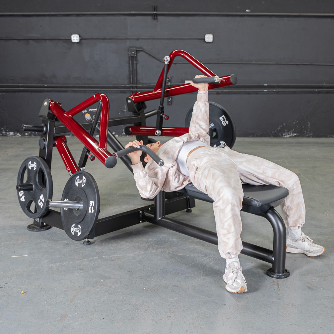 Woman using a red and black horizontal chest press machine with weight plates in a gym.