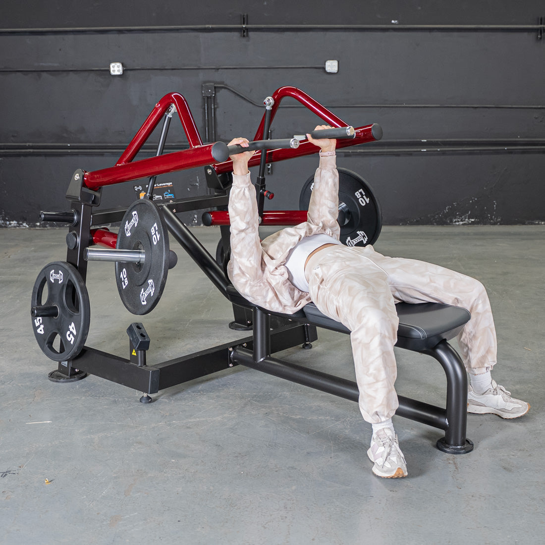 Person using a red and black horizontal chest press machine with weight plates.