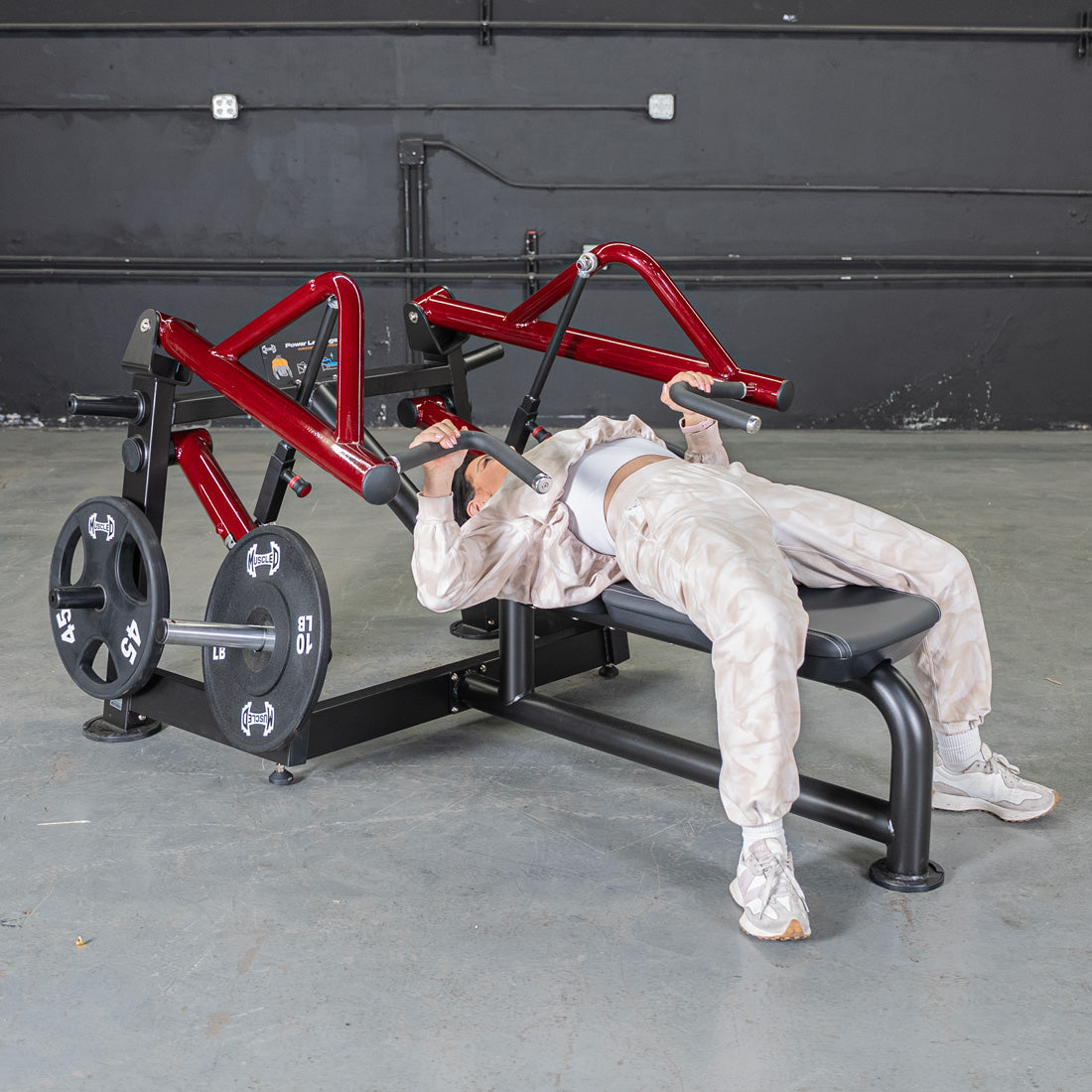 Person using a red and black horizontal chest press machine with weight plates in a gym.