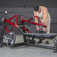 Thumbnail for Man loading a weight plate onto a red and black horizontal chest press machine in a gym.