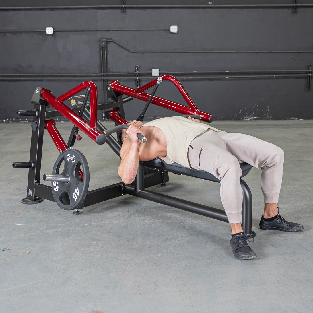 Man using a red and black horizontal chest press machine with a 45lb weight plate.