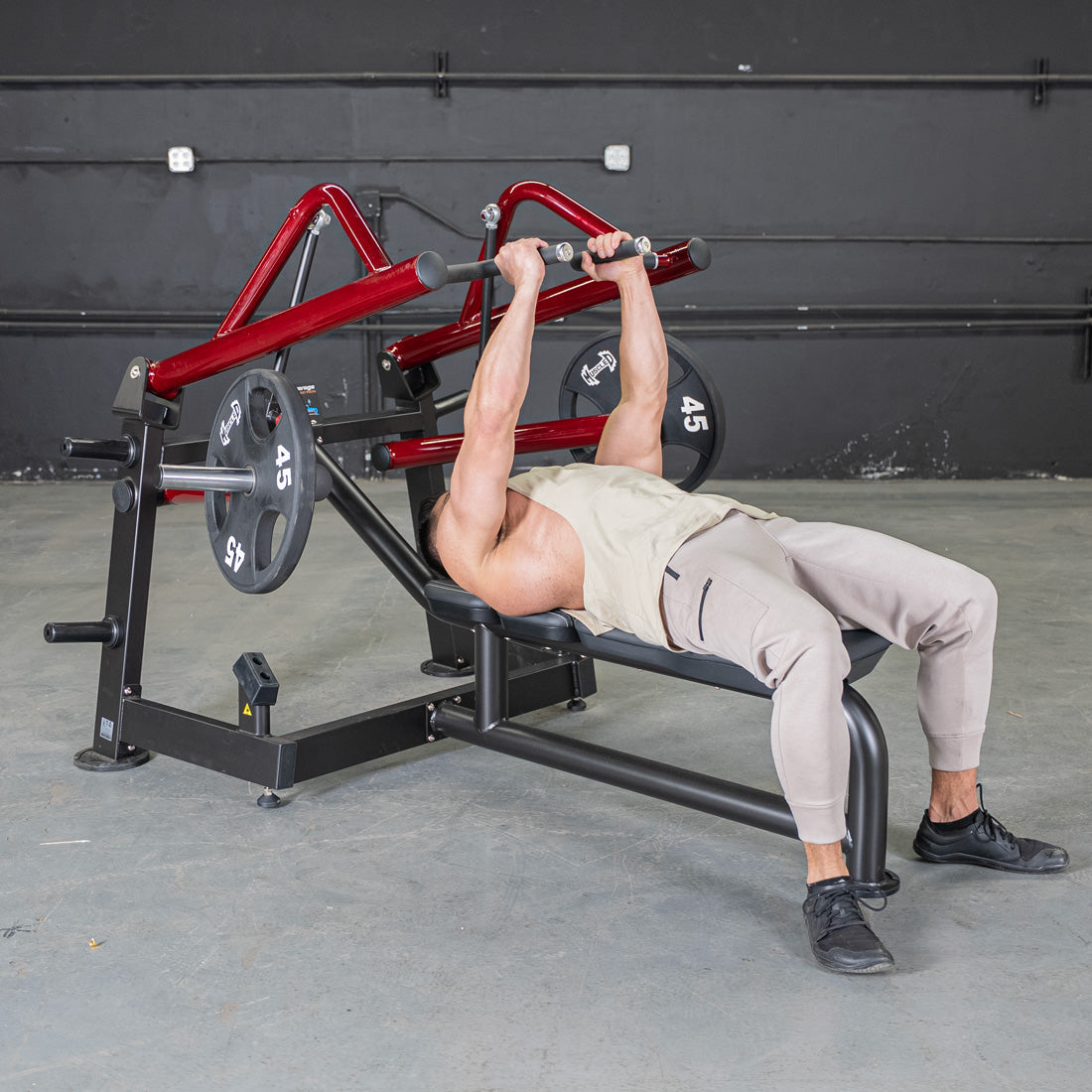 Man in a tank top and sweatpants using a red and black horizontal chest press machine with weights.