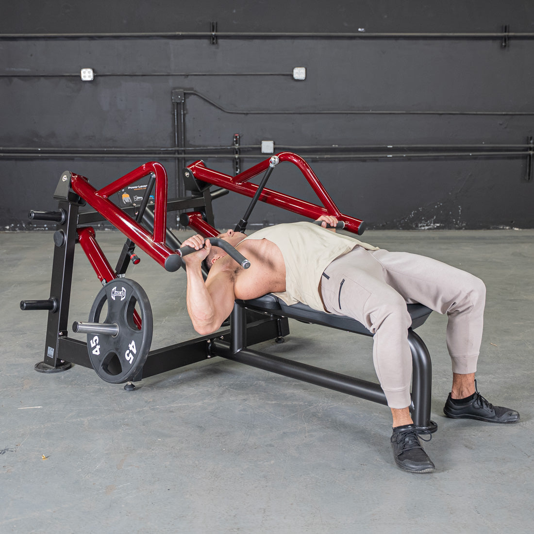 Man using a red and black horizontal chest press machine with a 45lb weight plate.