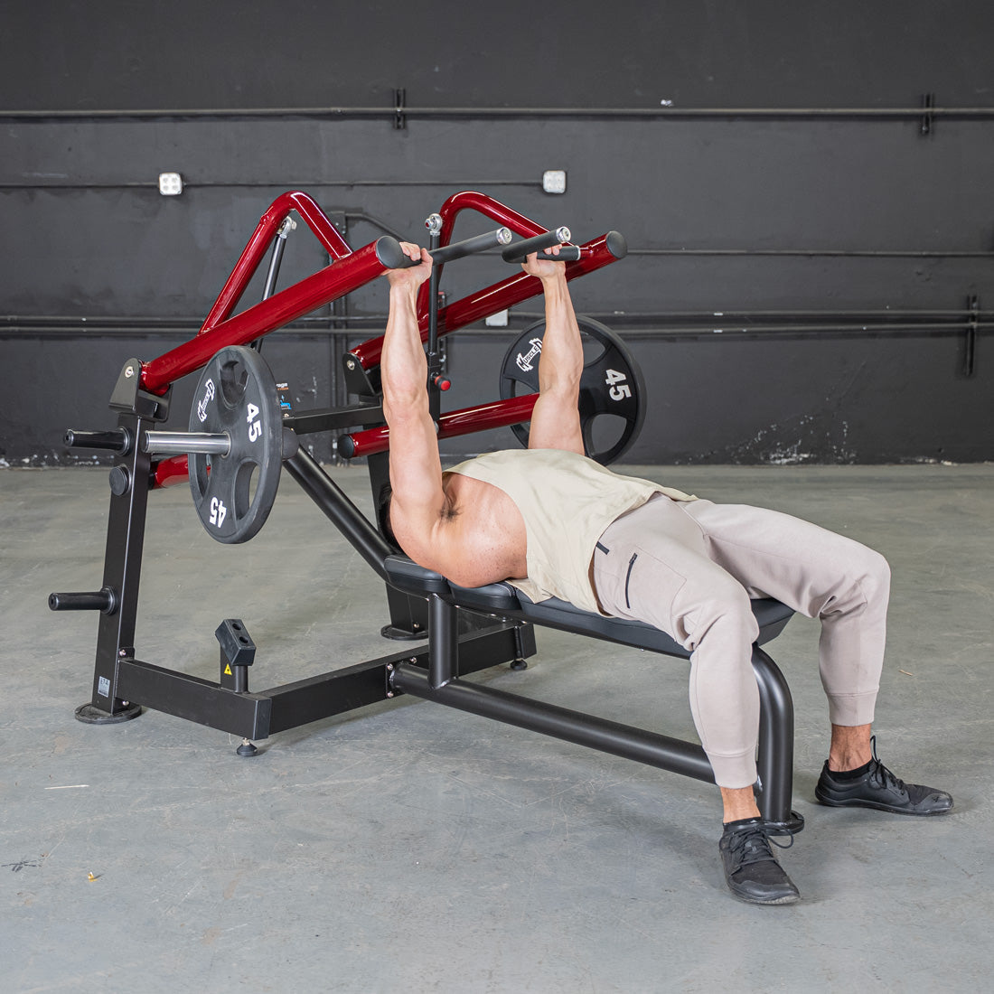 Man using a red and black horizontal chest press machine with weight plates.