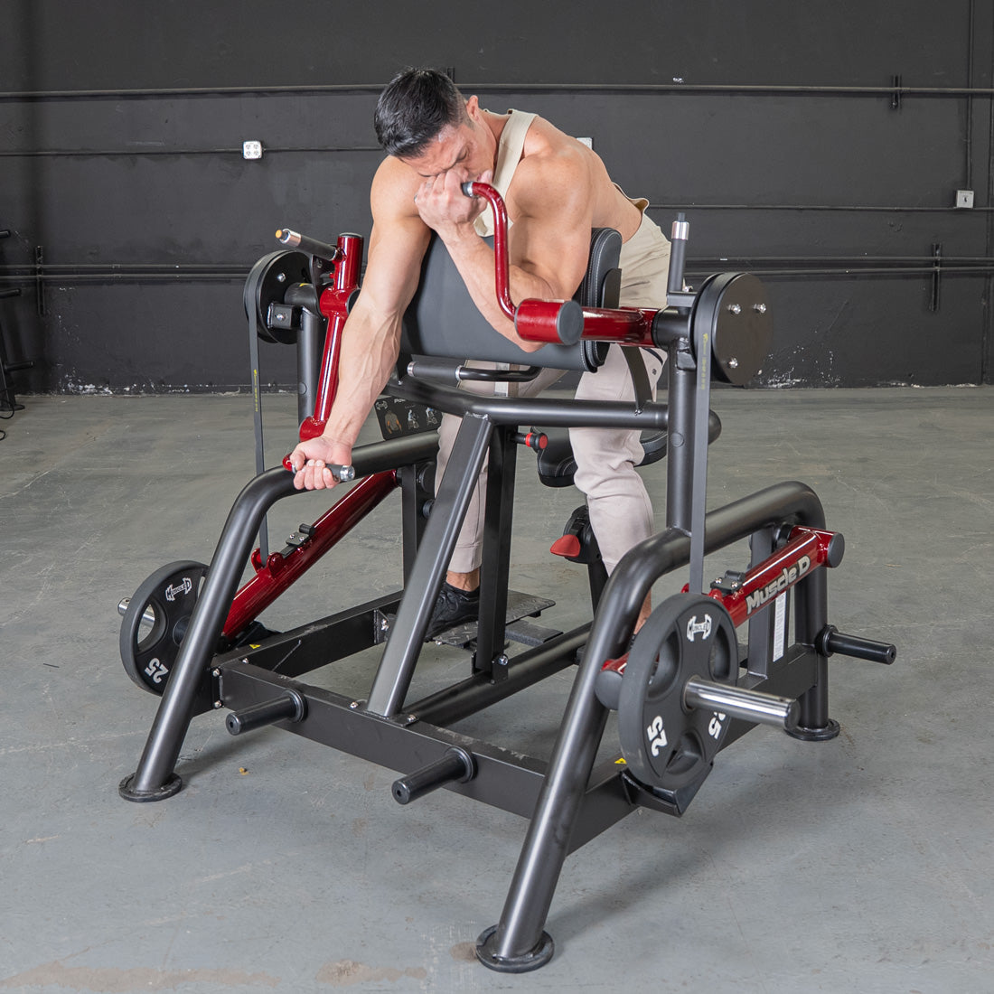 Man using a red and black biceps curl machine with 25lb weight plates in a gym.