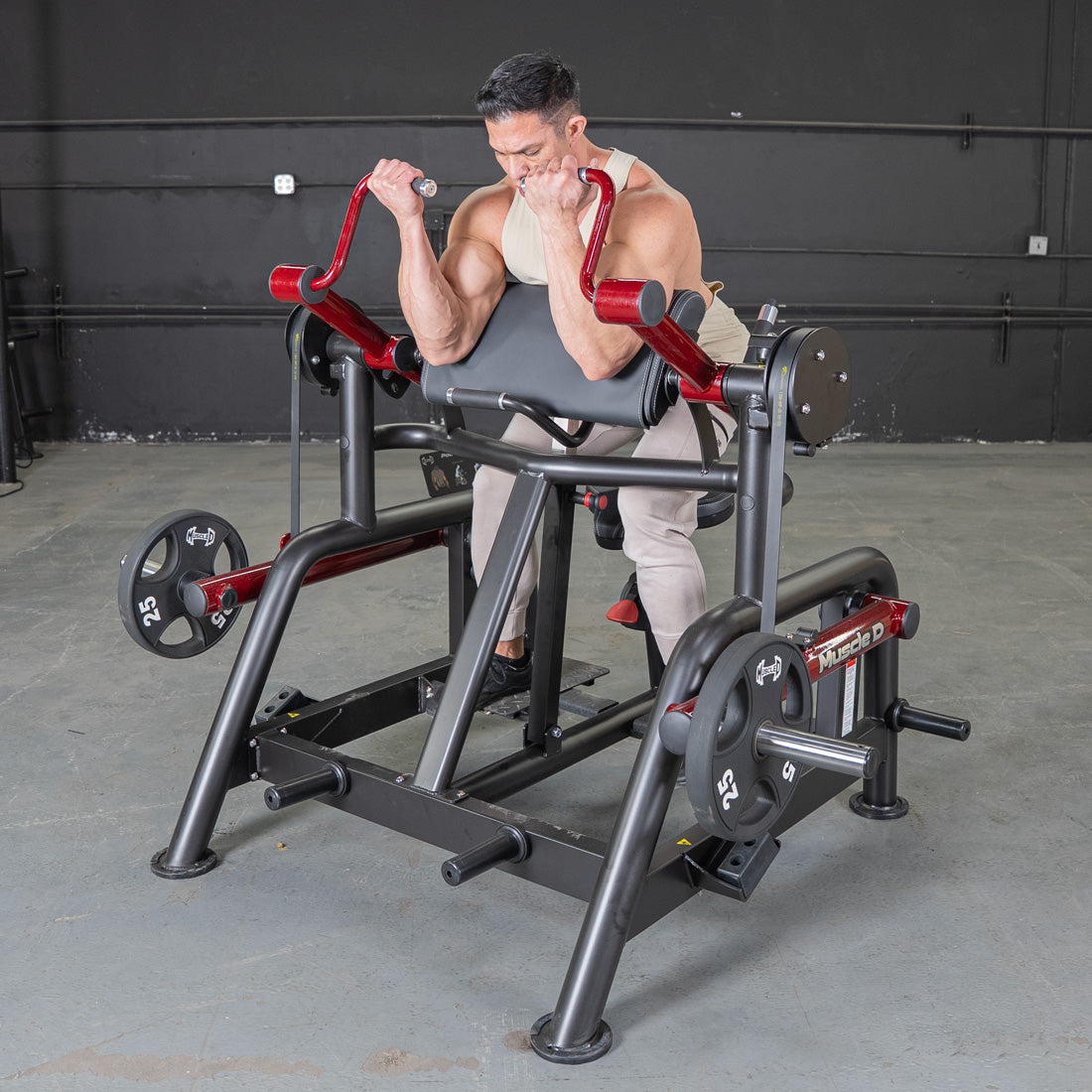 Man using a black and red biceps curl machine with weight plates in a gym.