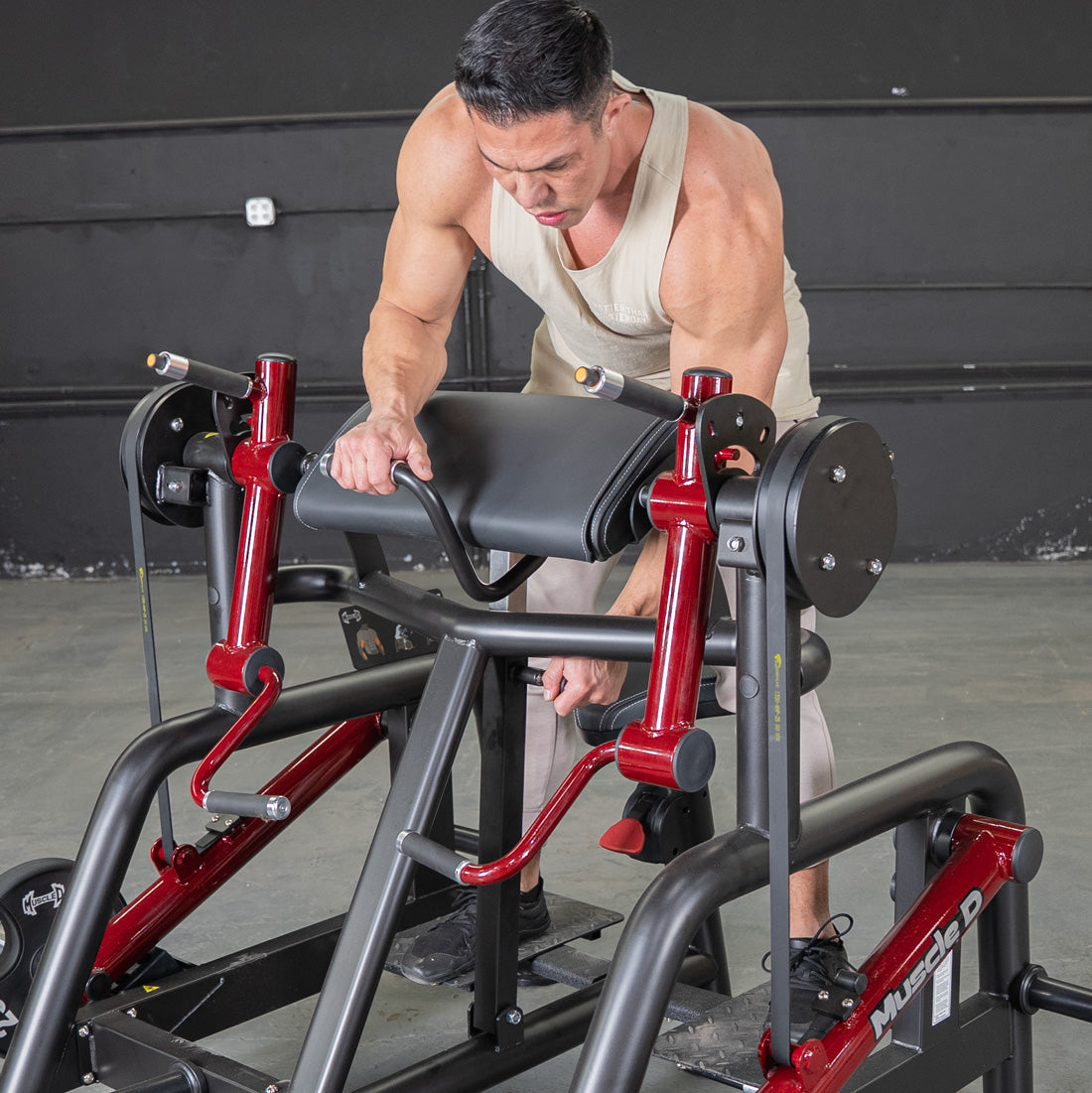 Man adjusting a red and black biceps curl machine with a padded armrest.