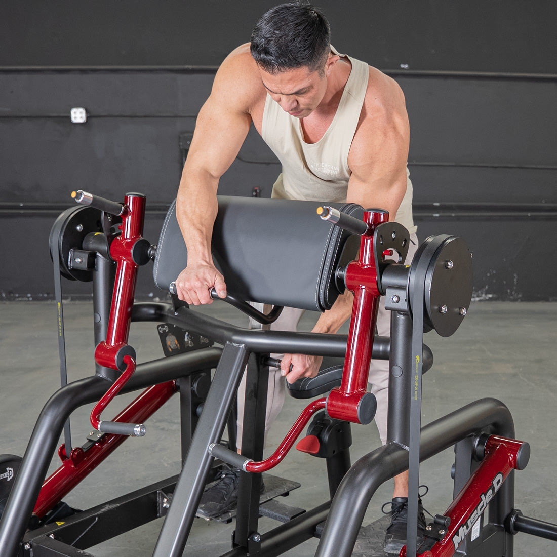 Man adjusting a black and red biceps curl machine with a padded armrest.