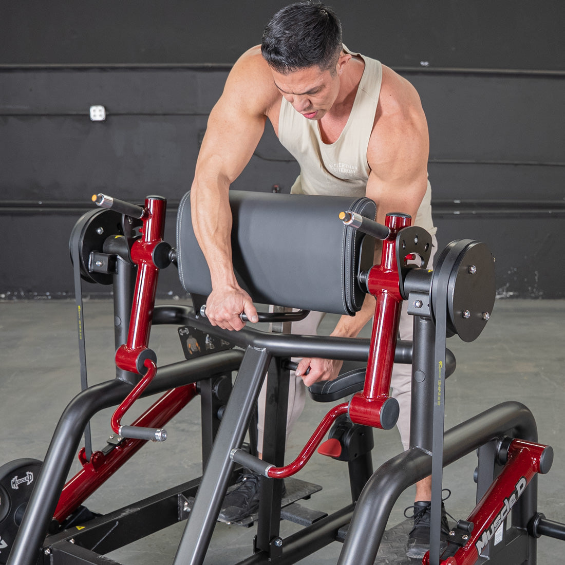 Man adjusting a red and black biceps curl machine with a padded armrest.