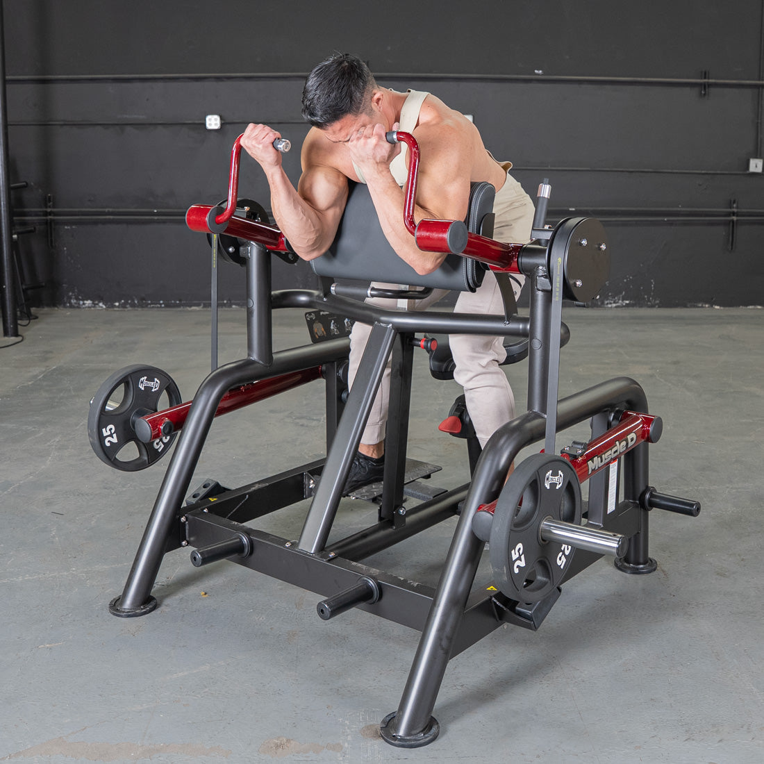 Man using a black and red biceps curl machine with 25lb weight plates in a gym.