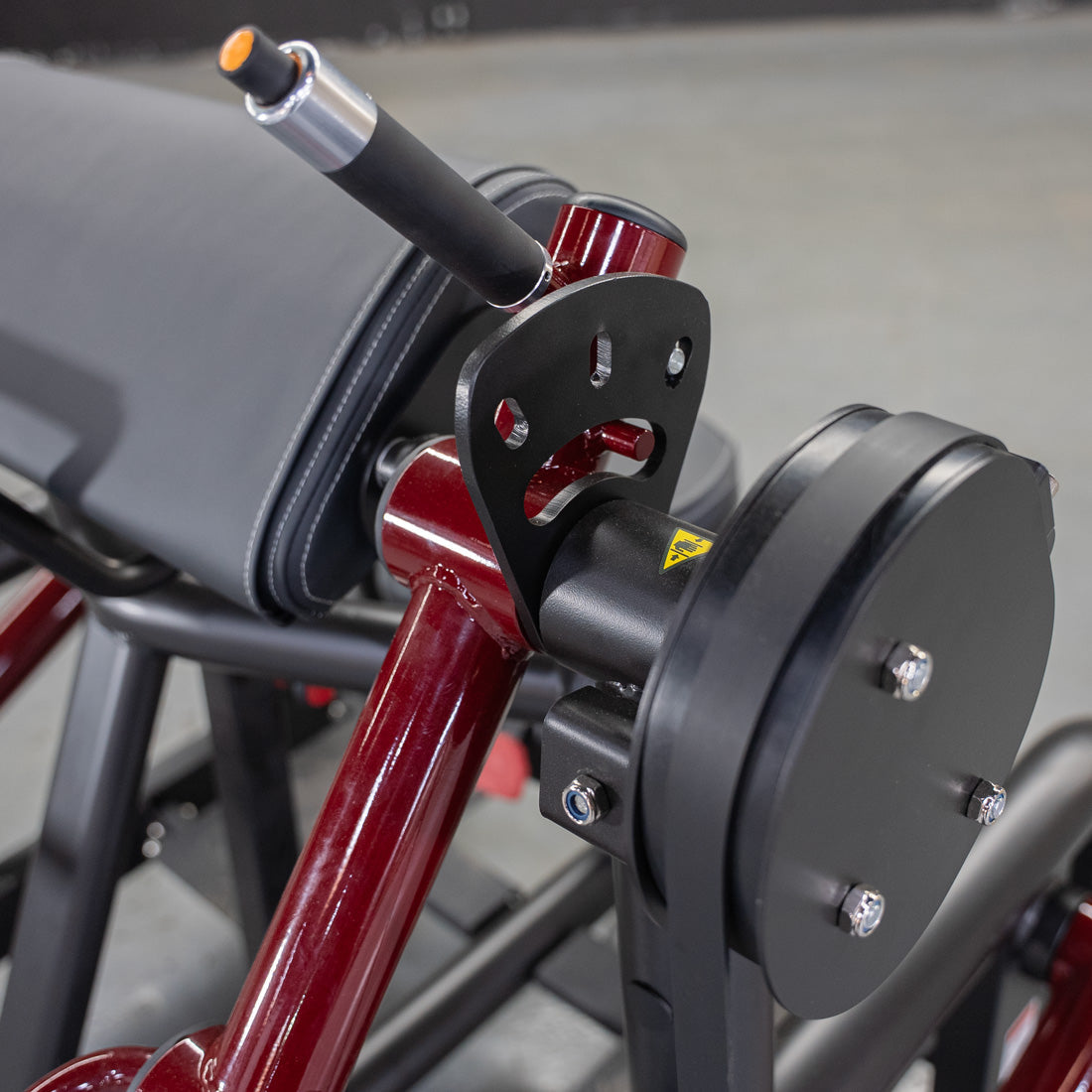 Close-up of a red and black biceps curl machine with a padded armrest and weight plate holder.