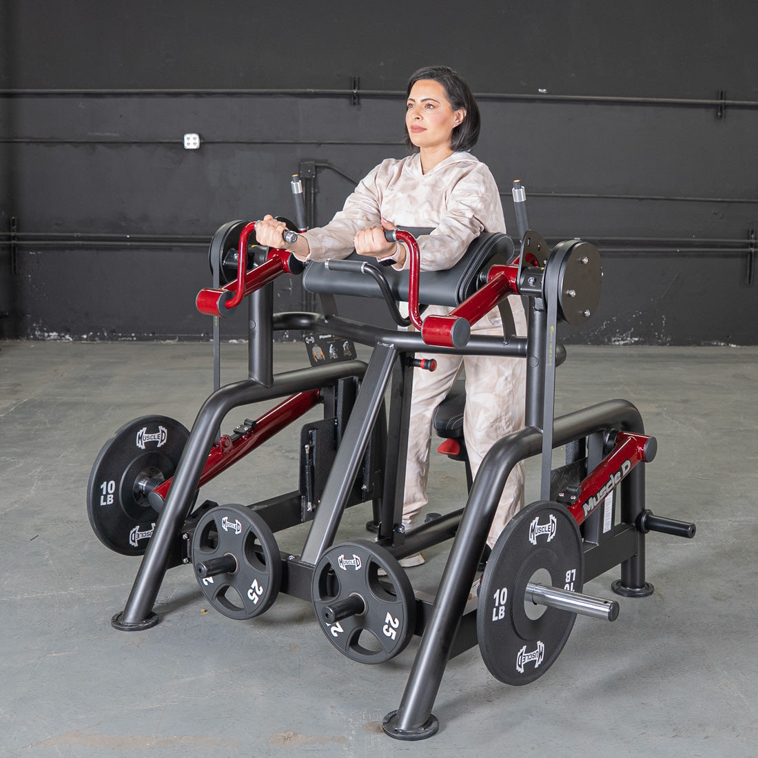 Woman using a black and red biceps curl machine with weight plates in a gym.