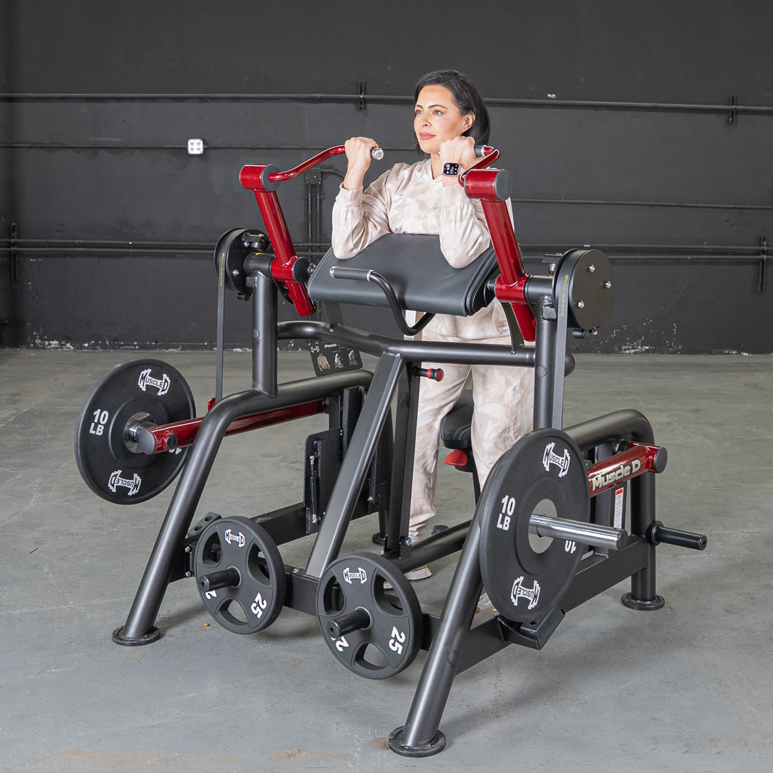 Woman using a black and red biceps curl machine with weight plates in a gym.