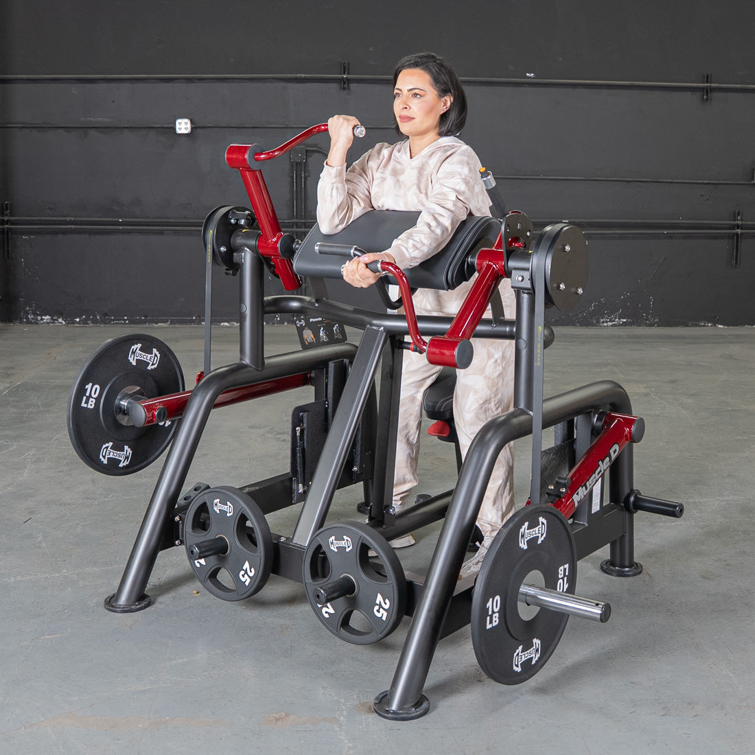 Woman using a black and red iso-lateral biceps curl machine with weight plates in a gym.