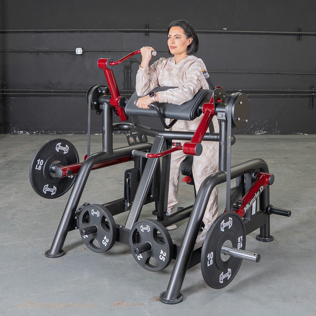 Woman using a black and red biceps curl machine with weight plates in a gym.