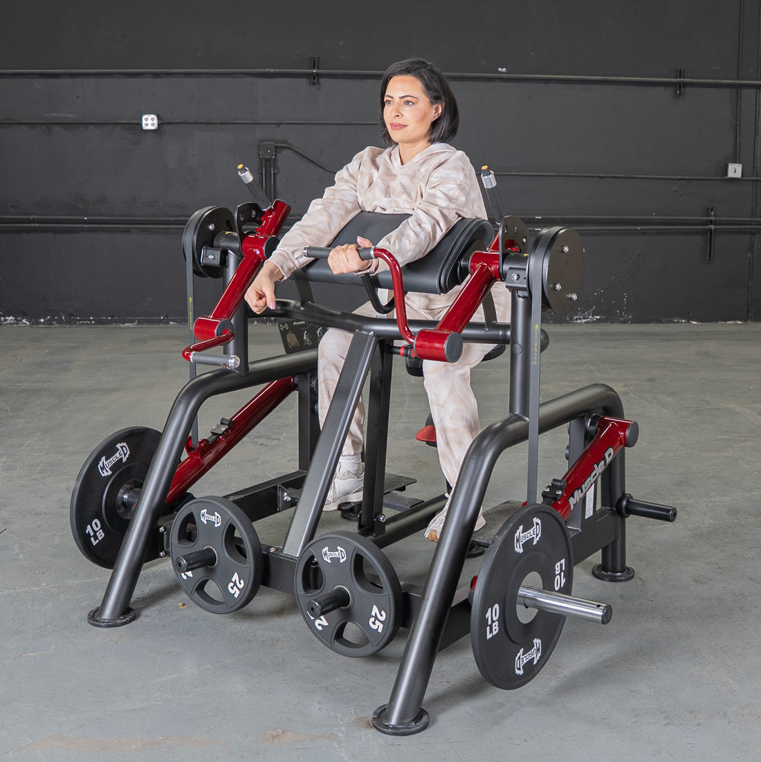 Woman using a black and red biceps curl machine with weight plates in a gym.