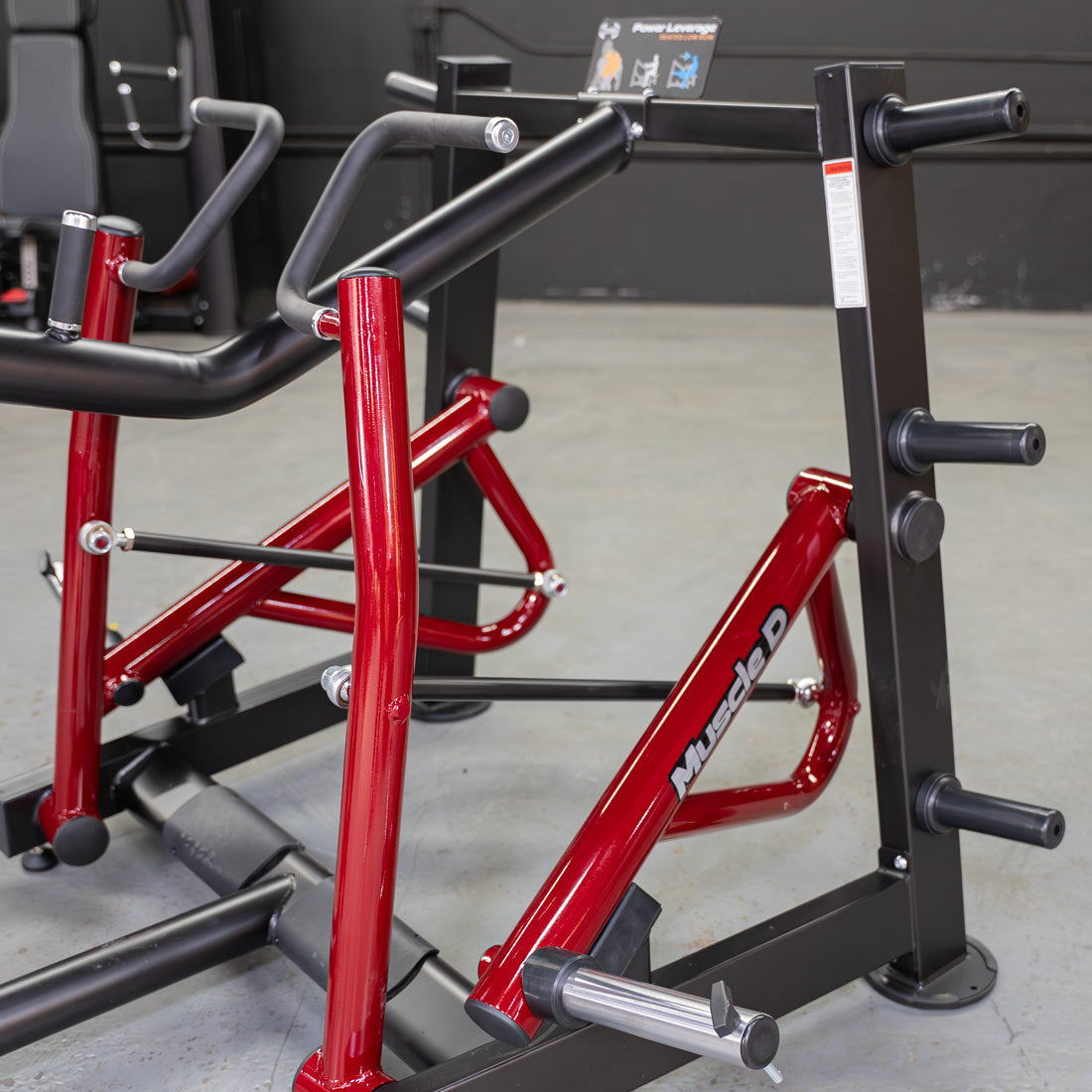 Close-up of a red and black iso-lateral seated row machine with "Muscle D" logo and weight plate holders.