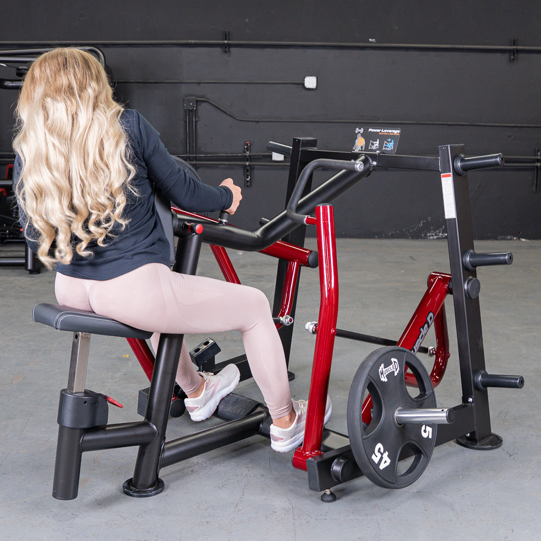 Woman with long blonde hair using a red and black iso-lateral seated row machine with a 45lb weight plate.