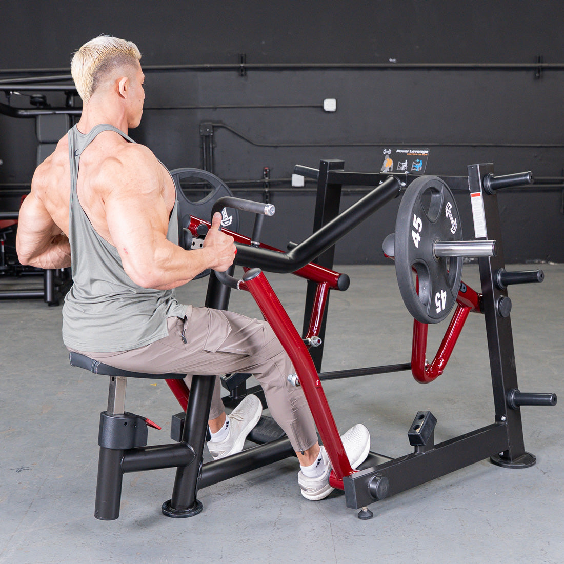 Muscular man using a red and black seated row machine with weight plates in a gym.