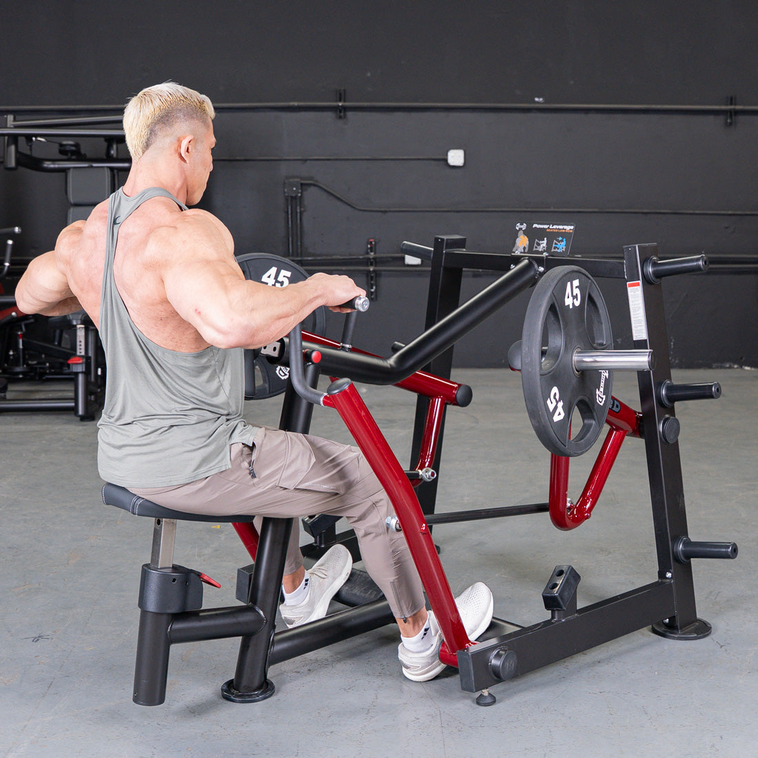 Muscular man using a black and red iso-lateral seated row machine with 45lb plates in a gym.