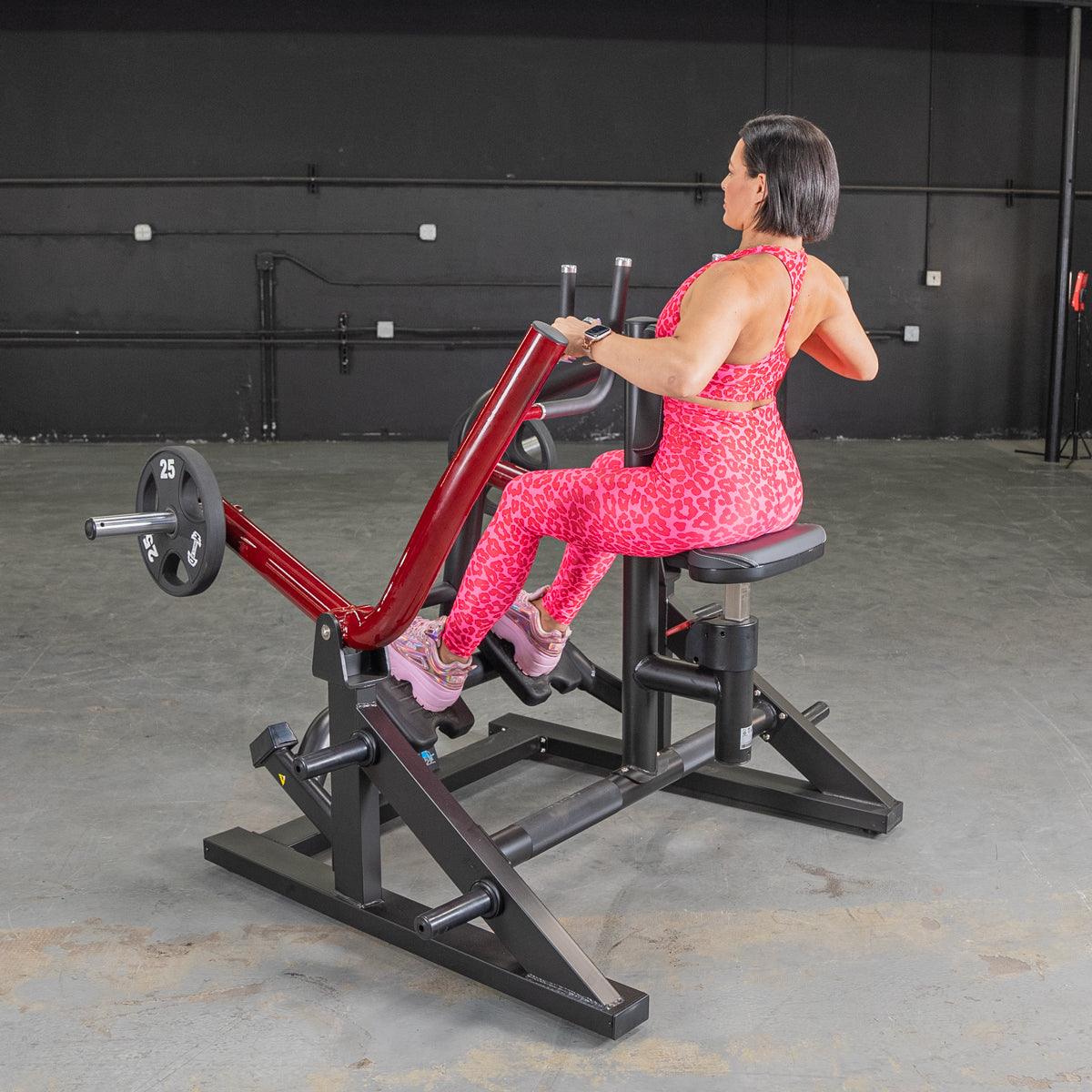Woman in pink leopard print using a red and black seated row machine with a 25lb weight plate.