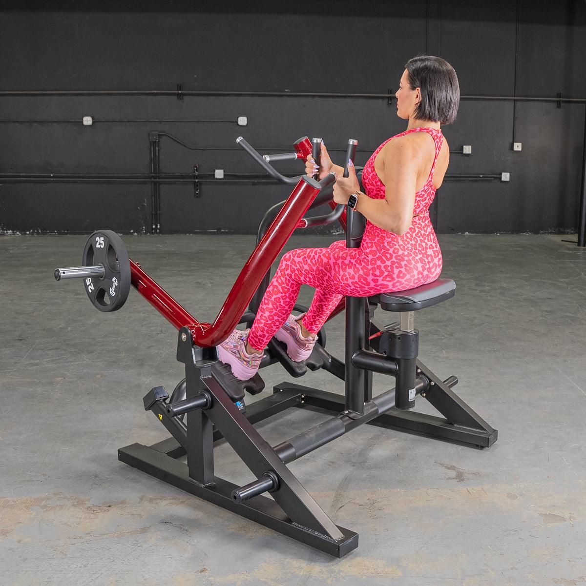 Woman in pink leopard print using a red and black seated row machine with a 25lb weight plate.