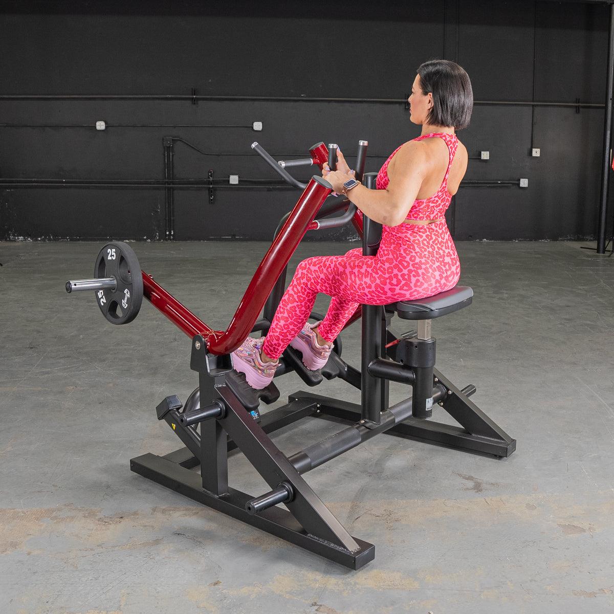 Woman in pink exercising on a red and black seated row machine with a 25lb weight plate.