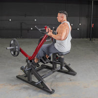 Thumbnail for Man in a tank top using a red and black seated row machine with a 45lb weight plate.