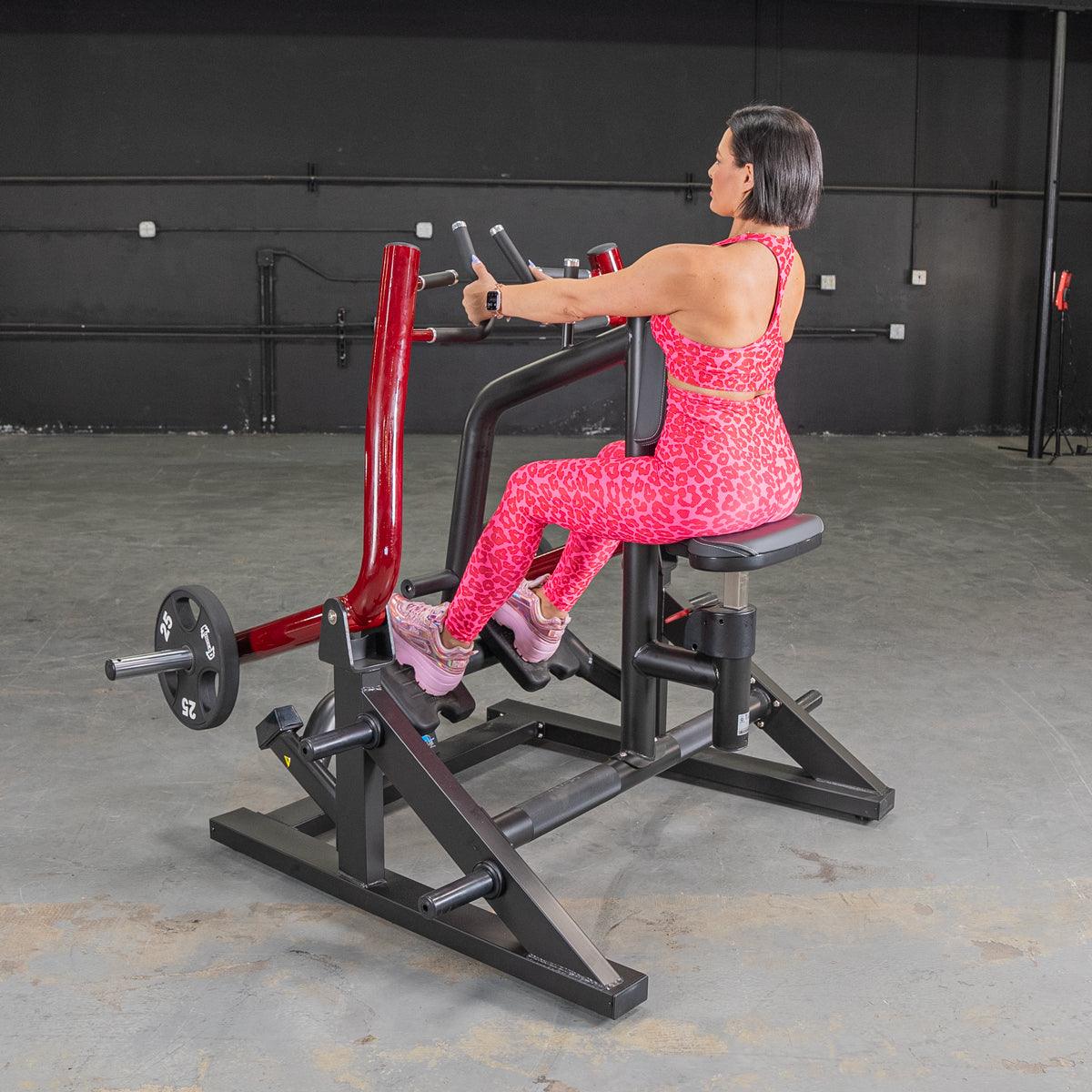 Woman in pink leopard print using a red and black seated row machine with a 25lb weight plate.