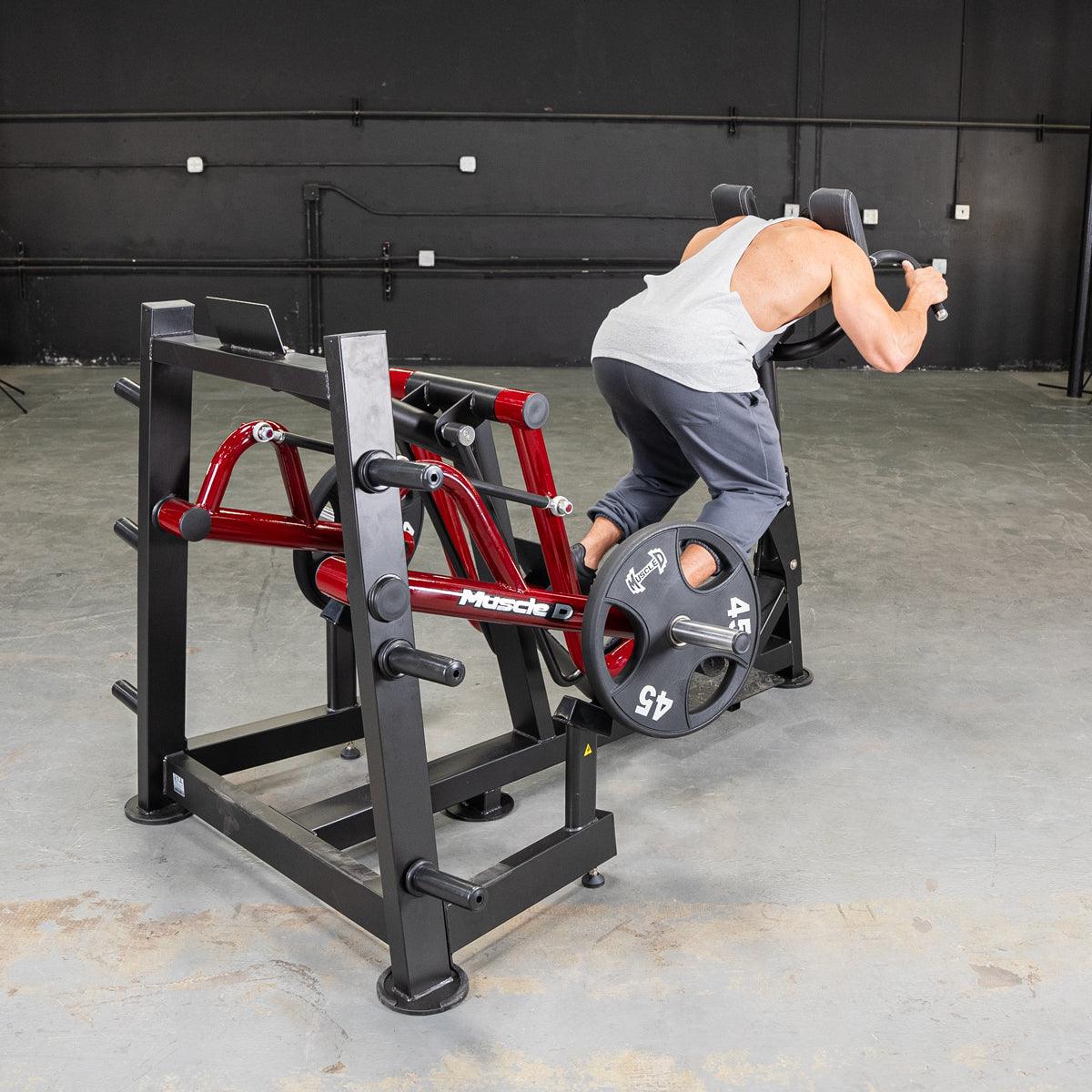 Man using a red and black iso lateral sprint trainer with a 45lb weight plate in a gym.