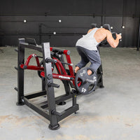 Thumbnail for Man using a red and black iso lateral sprint trainer with a 45lb weight plate in a gym.