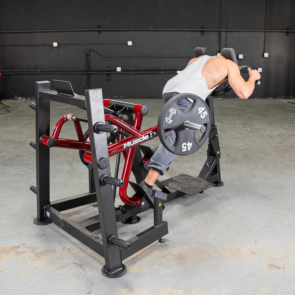Man using a red and black iso lateral sprint trainer with a 45lb weight plate in a gym.
