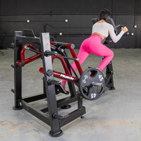 Thumbnail for Woman in pink leggings using a red and black iso-lateral sprint trainer with a 45lb weight plate.