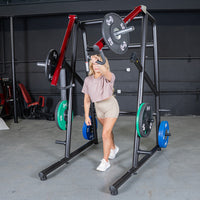 Thumbnail for Woman using a black and red jammer arm strength trainer with weight plates in a gym.