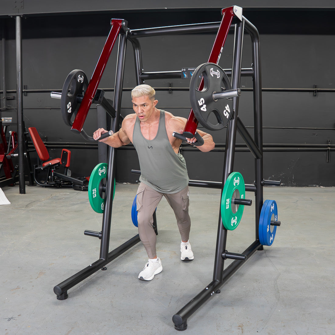 Man using a black and red jammer strength trainer with weight plates in a gym.