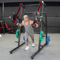Thumbnail for Man using a black and red jammer strength trainer with weight plates in a gym.