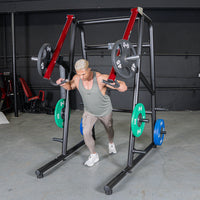 Thumbnail for Man using a black and red jammer strength trainer with weight plates in a gym.