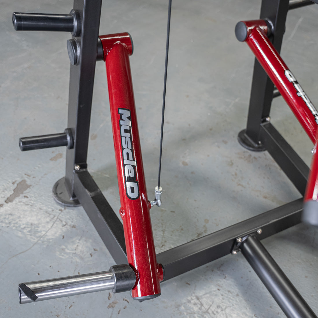 Red "Muscle D" fitness machine arm with cable and black frame on a gray floor.