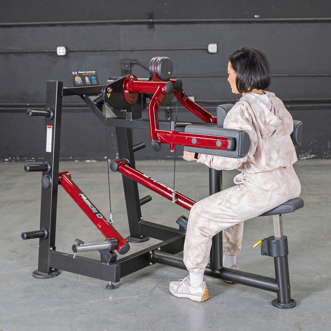 Woman using a red and black lateral raise machine in a gym.