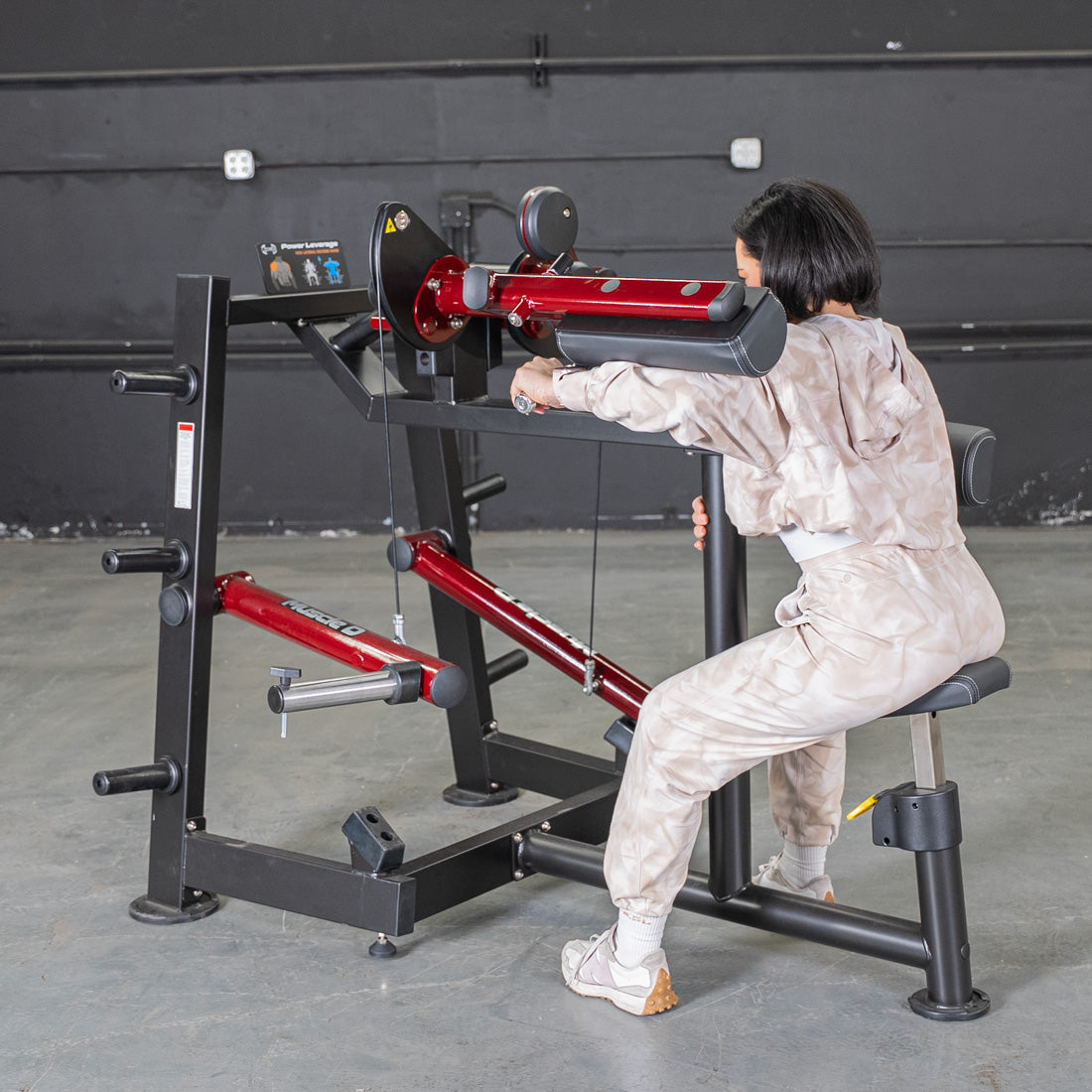 Woman using a red and black Power Leverage V2 Lateral Raise machine in a gym.