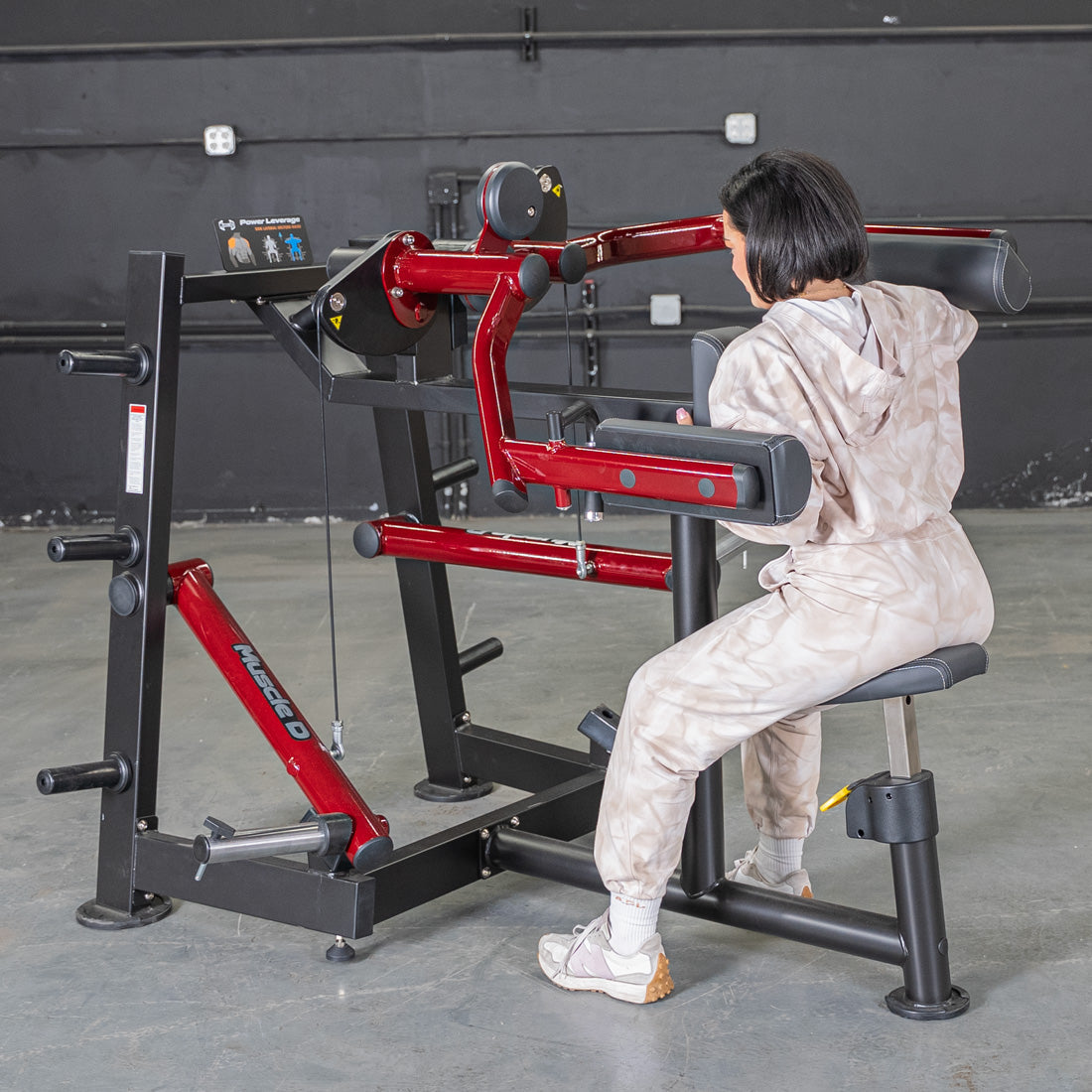 Woman using a red and black lateral raise machine in a gym.