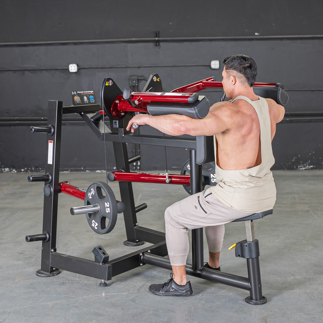 Man using a red and black lateral raise machine with 25lb weights in a gym.