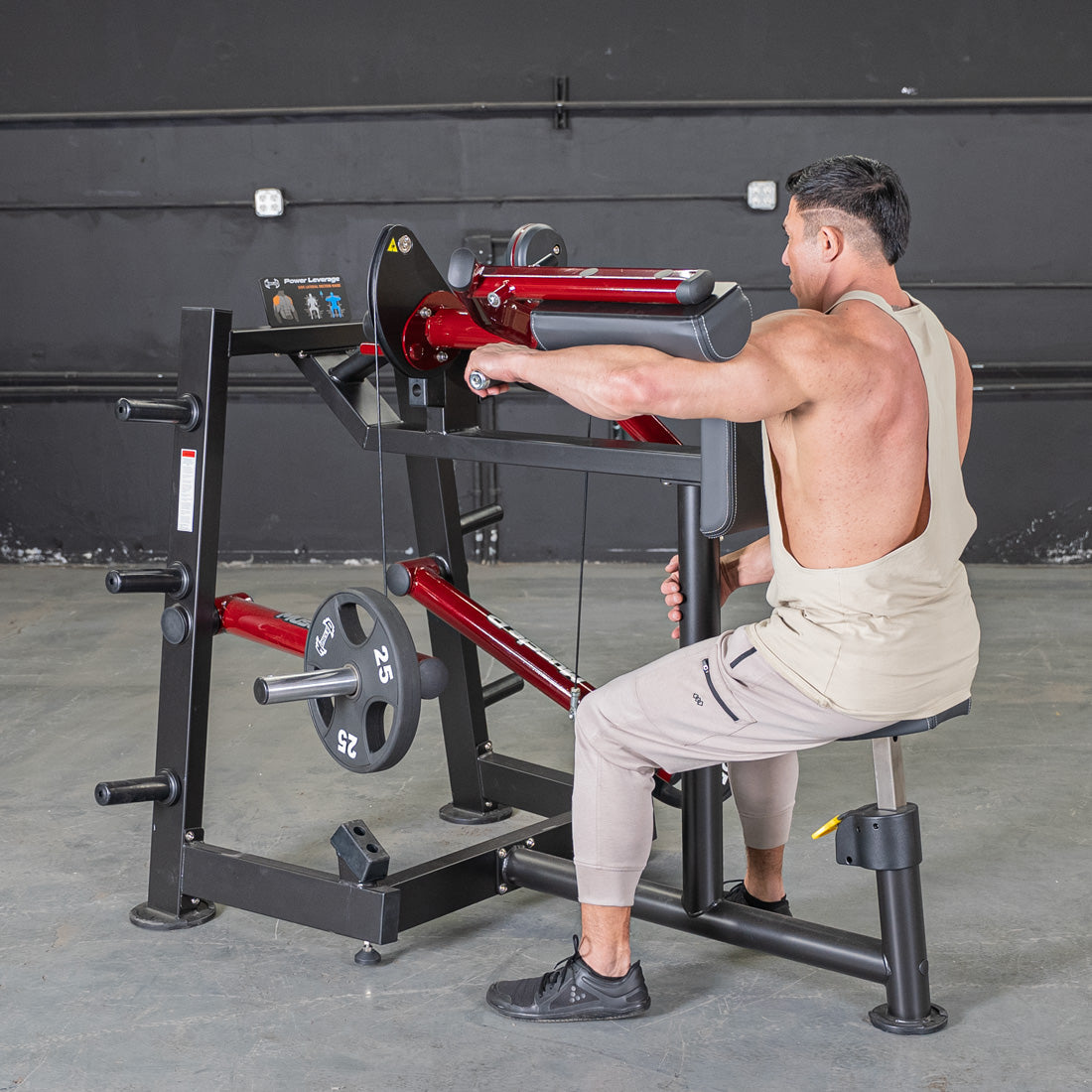 Man using a red and black lateral raise machine with a 25lb weight plate.