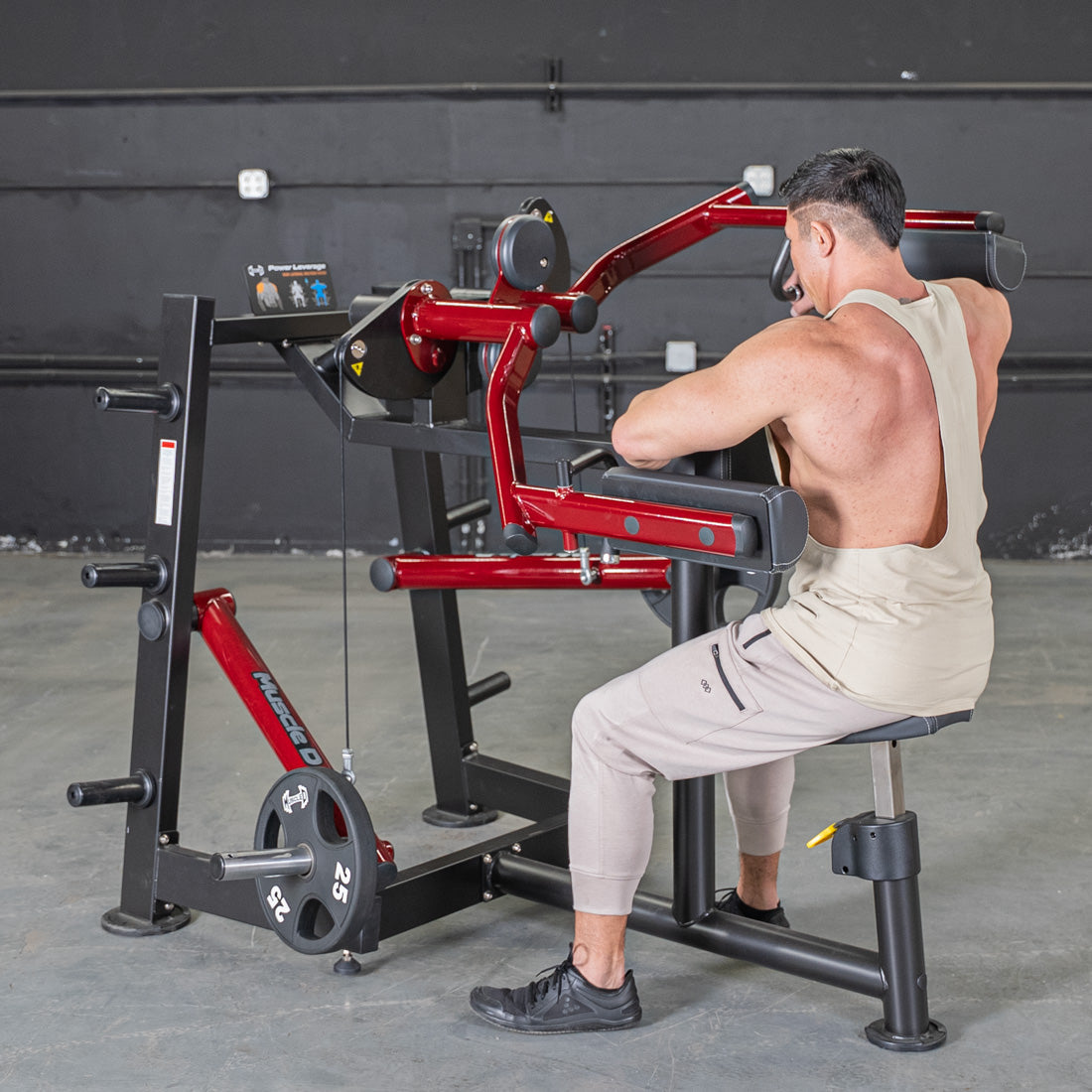 Man using a red and black lateral raise machine with 25lb weights in a gym.