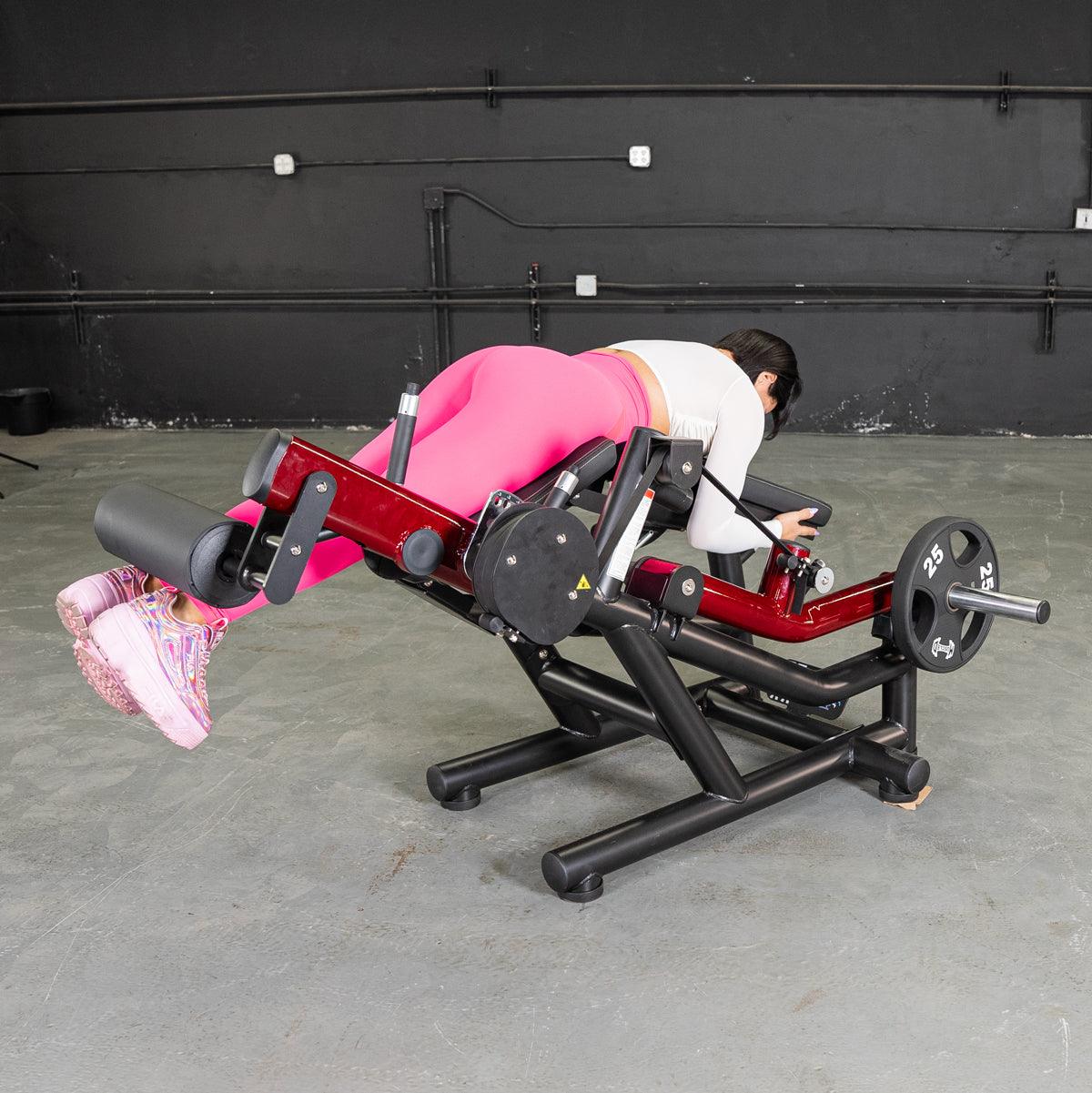 Woman in pink leggings using a red and black leg extension/curl machine with a 25lb weight plate.