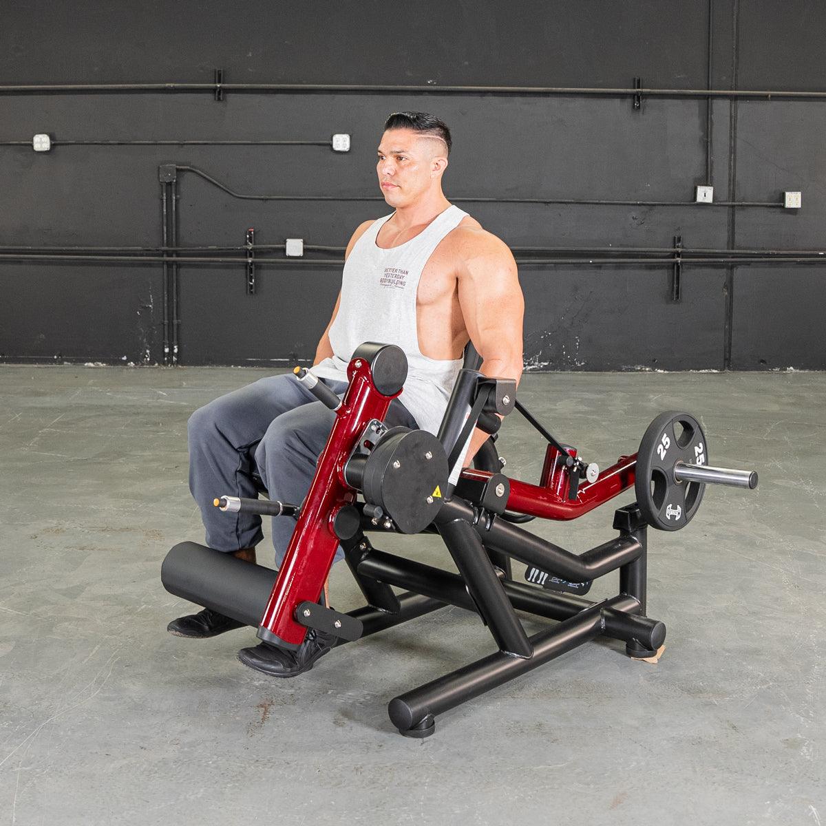 Man seated on a red and black leg extension/curl machine with a 25lb weight plate.