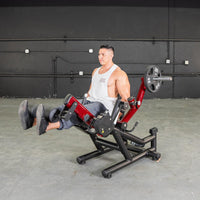 Thumbnail for Man in white tank top using a red and black leg extension machine with a 25lb weight plate.