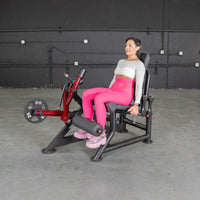 Thumbnail for Woman in pink leggings using a red and black leg extension machine with a 25lb weight plate.