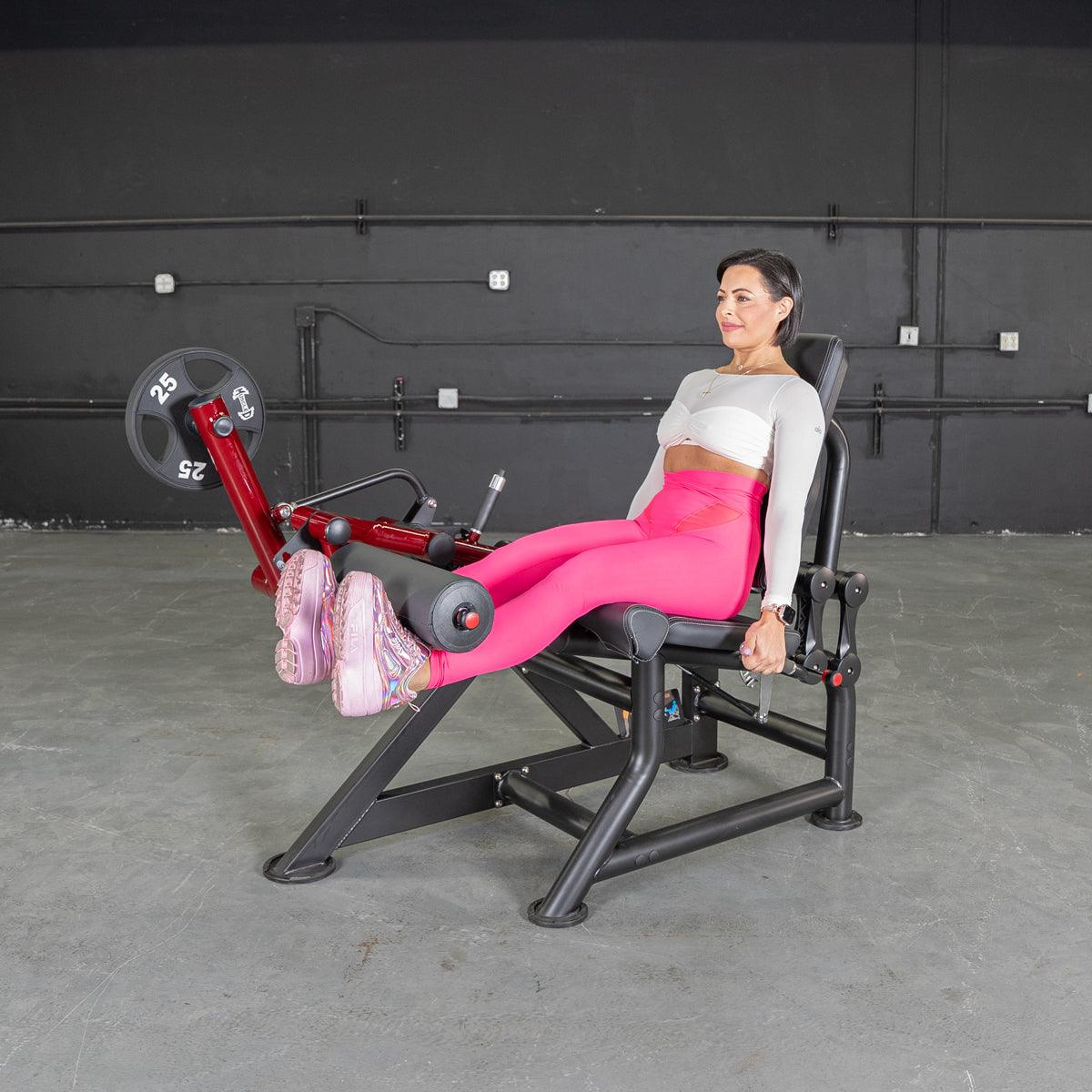 Woman in pink leggings using a red and black leg extension machine with a 25lb weight plate.
